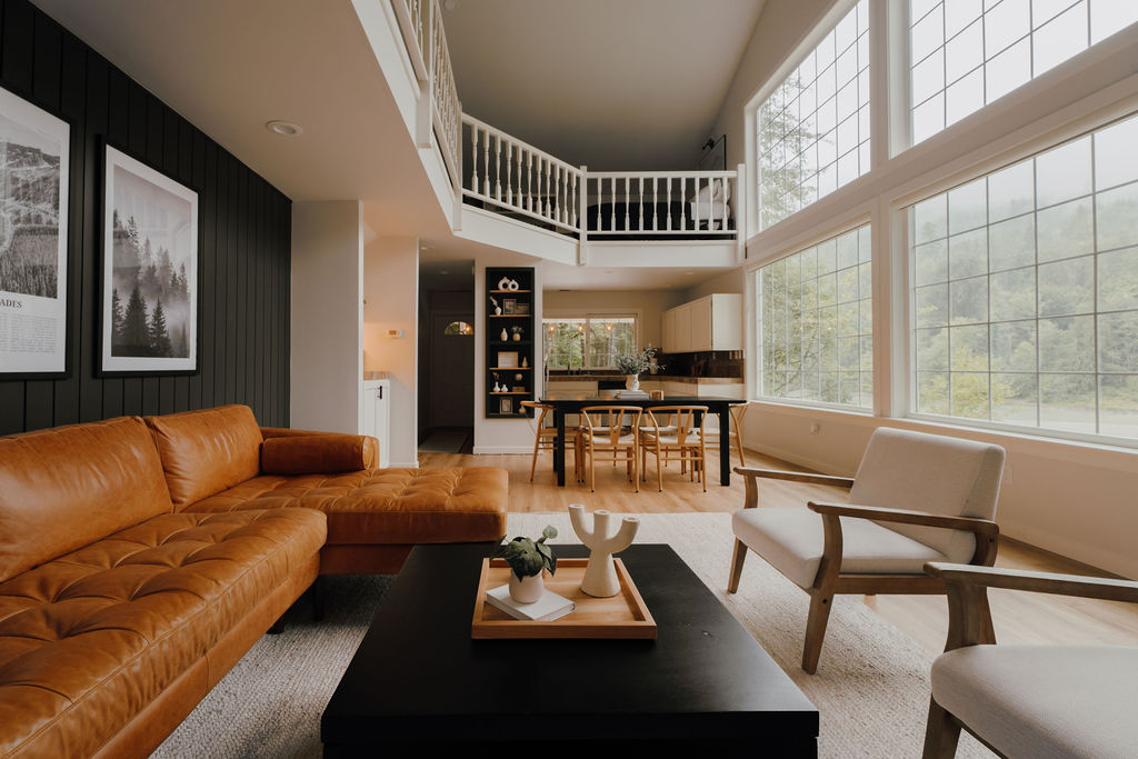 Completed open living room remodel with black accent wall, warm leather sofa, and large windows